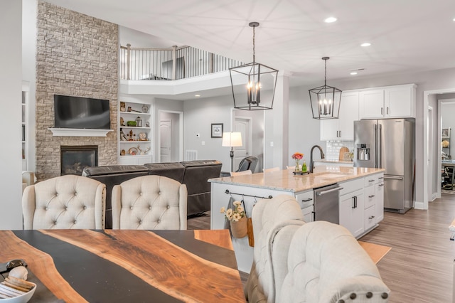 kitchen with stainless steel appliances, light stone countertops, an island with sink, and white cabinets