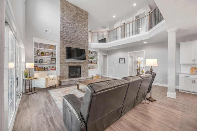 living room featuring ornate columns, built in features, a fireplace, and light hardwood / wood-style floors