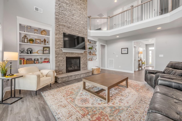 living room with built in shelves, a towering ceiling, wood-type flooring, and a fireplace