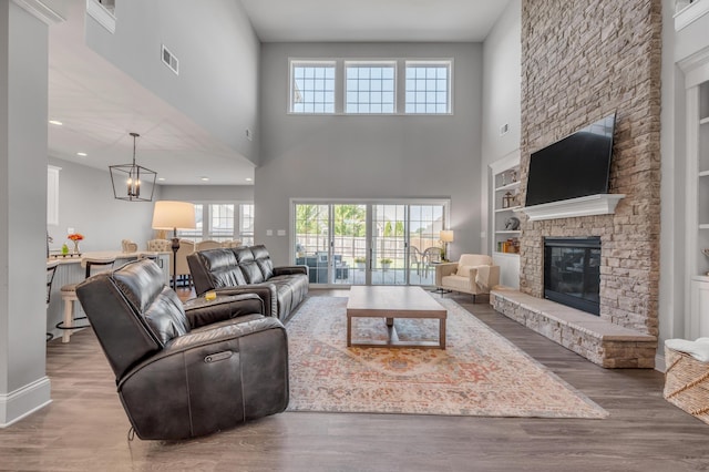 living room featuring an inviting chandelier, wood-type flooring, a stone fireplace, and built in features