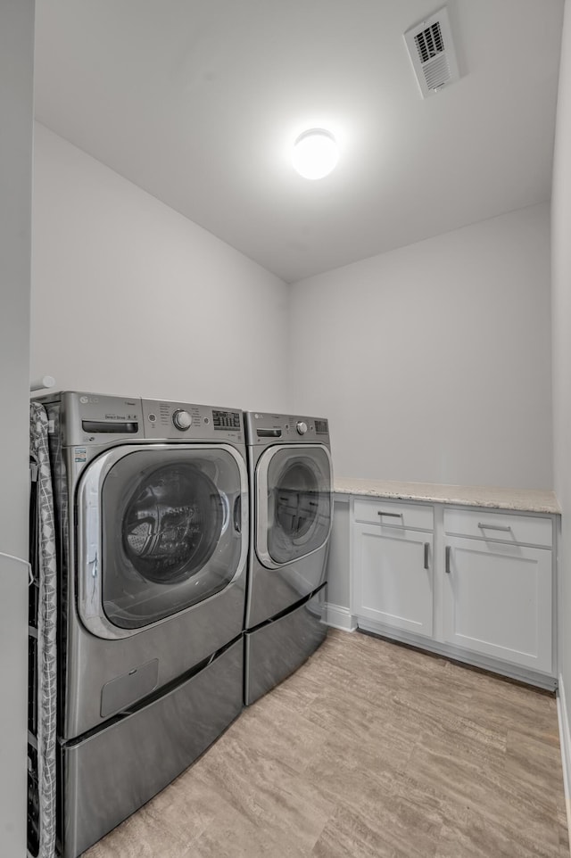 laundry room with cabinets, washer and clothes dryer, and light wood-type flooring