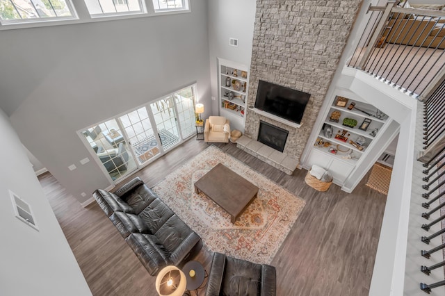 living room featuring a stone fireplace, wood-type flooring, built in features, and a towering ceiling