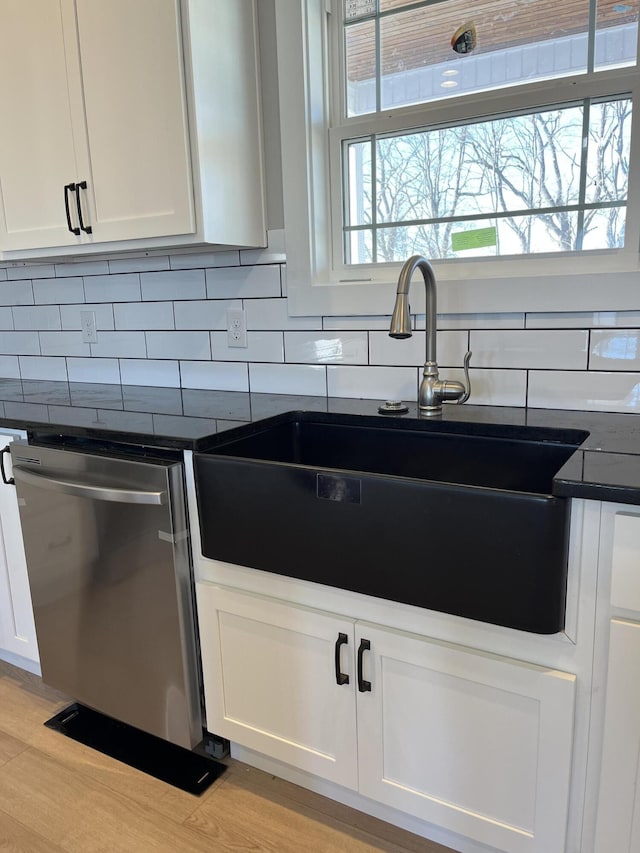 kitchen with a sink, stainless steel dishwasher, dark countertops, white cabinets, and decorative backsplash