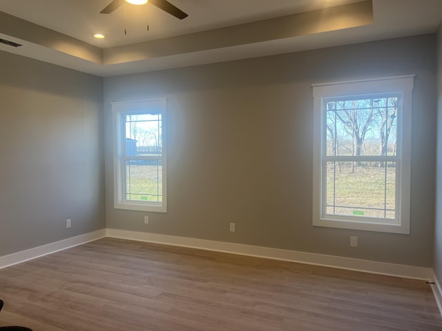 empty room with a tray ceiling, wood finished floors, baseboards, and visible vents