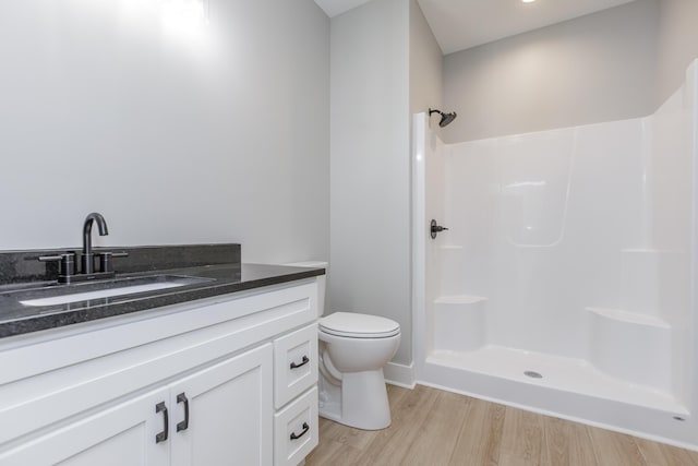 bathroom featuring toilet, wood finished floors, vanity, and walk in shower