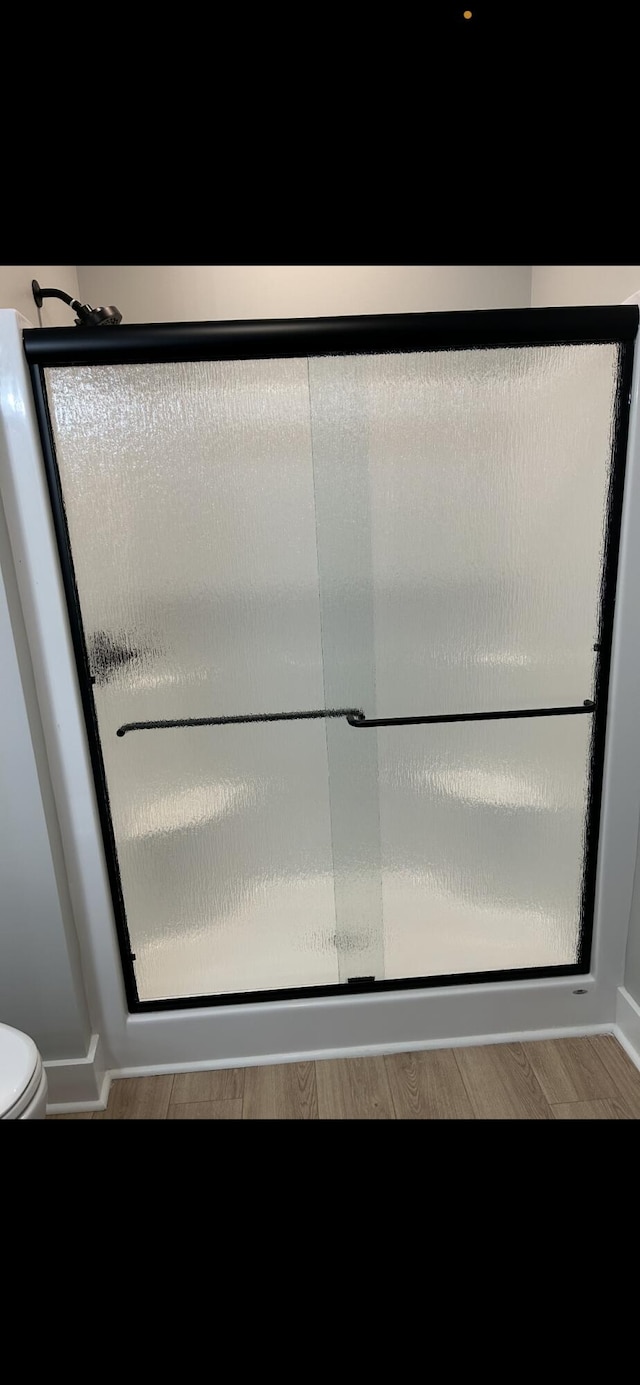 full bathroom with toilet, a stall shower, and wood finished floors
