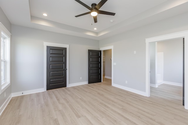 unfurnished bedroom with multiple windows, baseboards, light wood-type flooring, and a raised ceiling