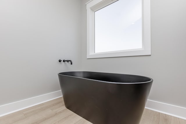 bathroom with baseboards, a freestanding bath, and wood finished floors
