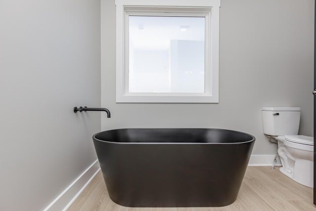 bathroom featuring toilet, baseboards, a freestanding bath, and wood finished floors