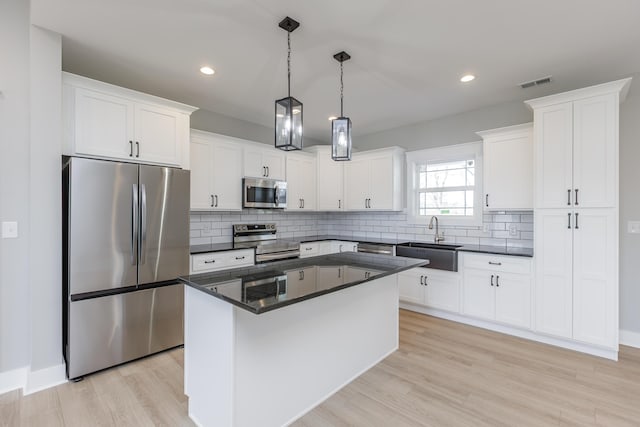 kitchen with light wood-style floors, visible vents, dark countertops, a sink, and stainless steel appliances