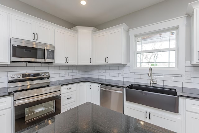kitchen featuring white cabinets, dark stone countertops, a sink, stainless steel appliances, and backsplash
