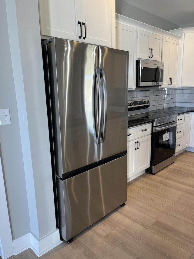 kitchen featuring backsplash, dark countertops, white cabinetry, light wood-style floors, and appliances with stainless steel finishes