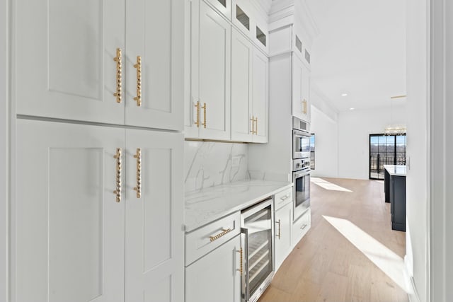 bar with wine cooler, white cabinetry, light stone counters, light wood-type flooring, and backsplash