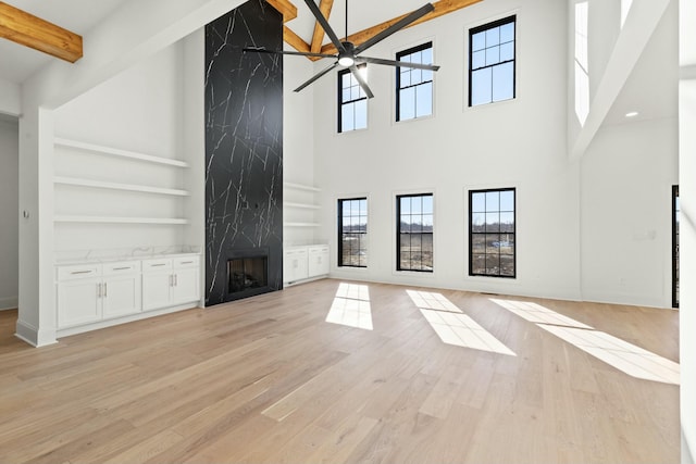 unfurnished living room with light hardwood / wood-style flooring, a premium fireplace, ceiling fan, built in shelves, and beamed ceiling