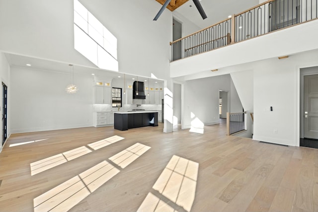 unfurnished living room featuring a towering ceiling, ceiling fan, and light hardwood / wood-style flooring