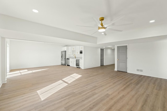 unfurnished living room featuring sink, beverage cooler, ceiling fan, and light hardwood / wood-style flooring