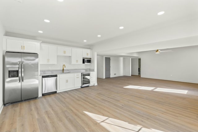 kitchen with sink, light hardwood / wood-style flooring, white cabinetry, stainless steel appliances, and beverage cooler