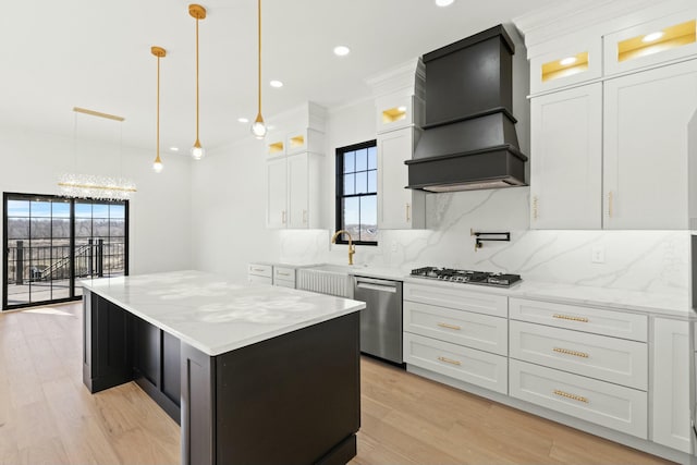 kitchen with premium range hood, appliances with stainless steel finishes, decorative light fixtures, white cabinetry, and a center island