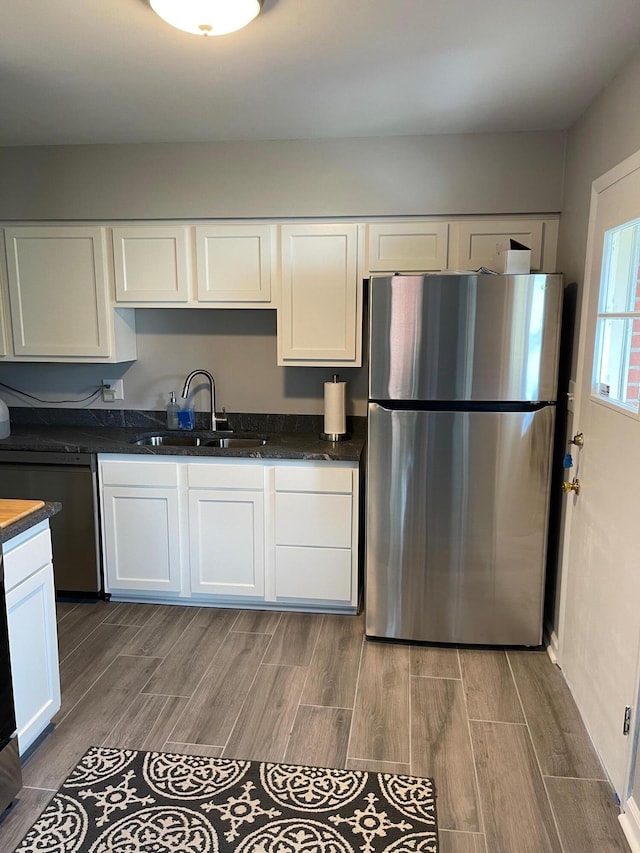 kitchen with sink, white cabinetry, stainless steel refrigerator, dishwasher, and dark stone counters