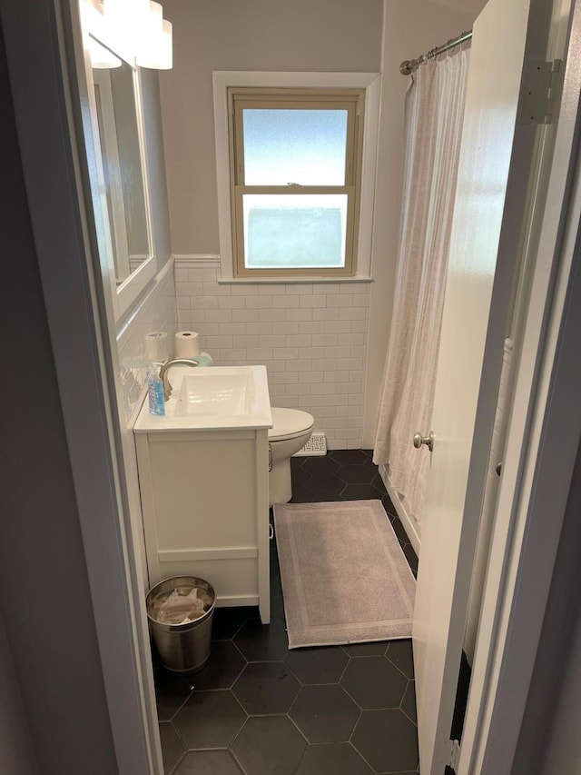 bathroom with toilet, a wainscoted wall, tile patterned flooring, vanity, and tile walls