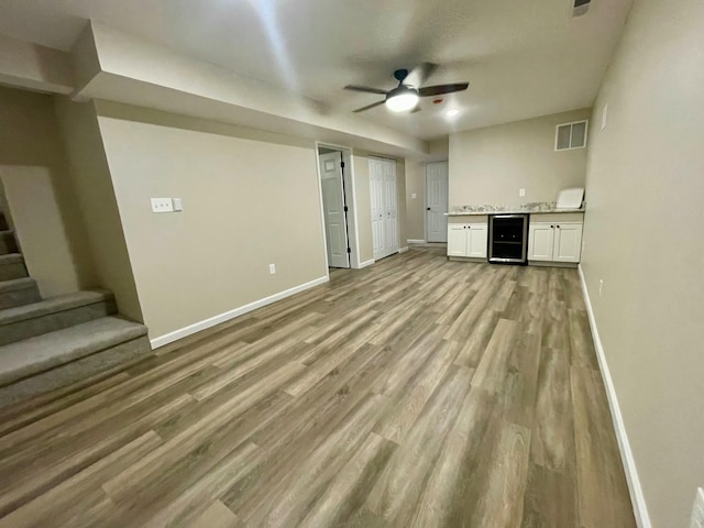 unfurnished living room with indoor bar, beverage cooler, ceiling fan, and light wood-type flooring