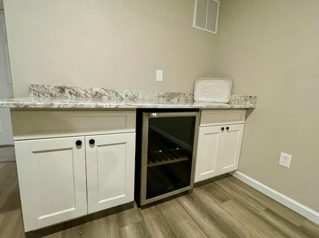 bar with light hardwood / wood-style flooring, light stone countertops, beverage cooler, and white cabinets