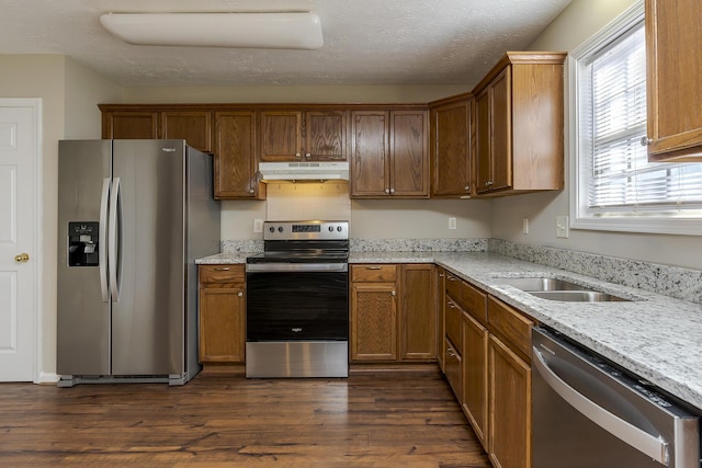 kitchen with sink, stainless steel appliances, dark hardwood / wood-style floors, light stone countertops, and a textured ceiling