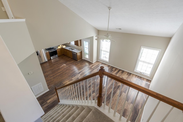 staircase featuring hardwood / wood-style flooring, vaulted ceiling, ceiling fan, and a textured ceiling