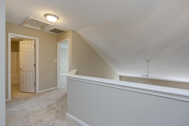 corridor with vaulted ceiling, light carpet, and a textured ceiling