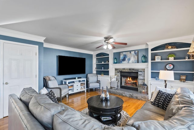 living room featuring crown molding, wood-type flooring, a stone fireplace, and built in shelves