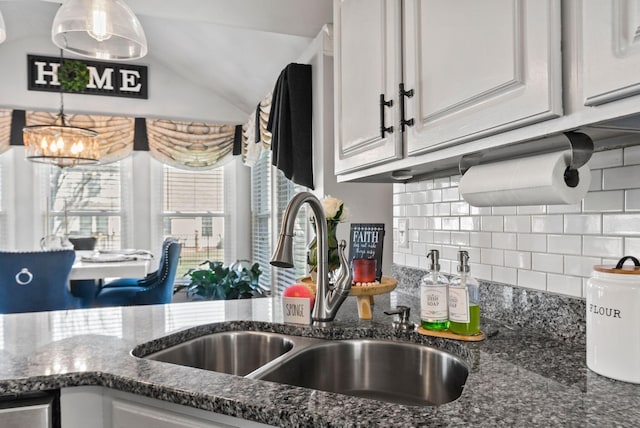 kitchen with tasteful backsplash, white cabinetry, sink, and dark stone counters