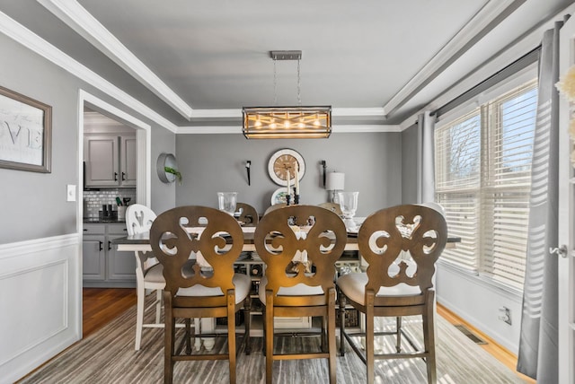 dining area with crown molding, light hardwood / wood-style floors, and a raised ceiling