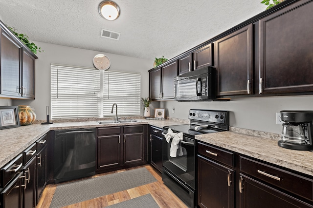 kitchen with sink, light wood-type flooring, black appliances, dark brown cabinets, and a textured ceiling