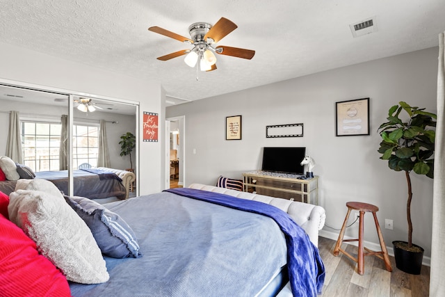 bedroom featuring ceiling fan, a textured ceiling, light hardwood / wood-style floors, and a closet