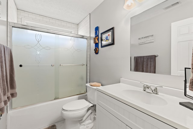 full bathroom with bath / shower combo with glass door, vanity, a textured ceiling, and toilet