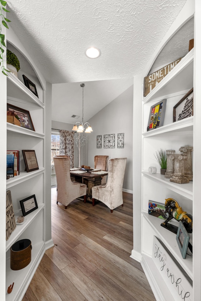 dining space featuring hardwood / wood-style flooring, lofted ceiling, a notable chandelier, and a textured ceiling