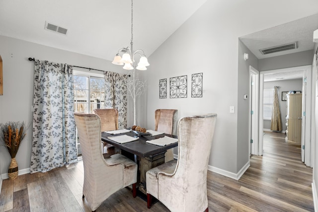 dining room with hardwood / wood-style flooring, vaulted ceiling, and a notable chandelier