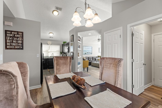 dining room featuring ceiling fan with notable chandelier, sink, hardwood / wood-style floors, and a textured ceiling