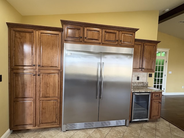 kitchen with wine cooler, lofted ceiling, light tile patterned floors, built in fridge, and stone counters