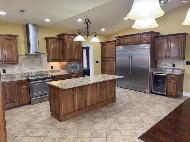 kitchen with wine cooler, light stone counters, built in appliances, a kitchen island, and wall chimney range hood