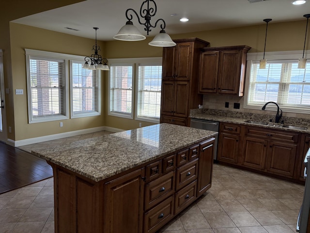 kitchen featuring sink, light stone counters, a wealth of natural light, a kitchen island, and decorative light fixtures