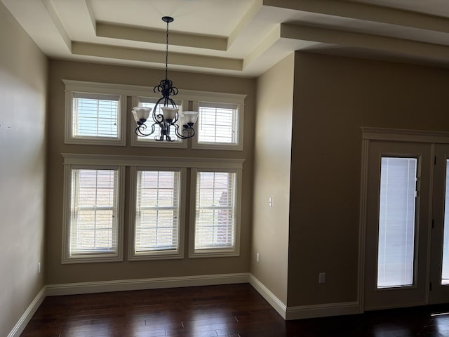 unfurnished dining area with a notable chandelier, dark hardwood / wood-style floors, and a raised ceiling