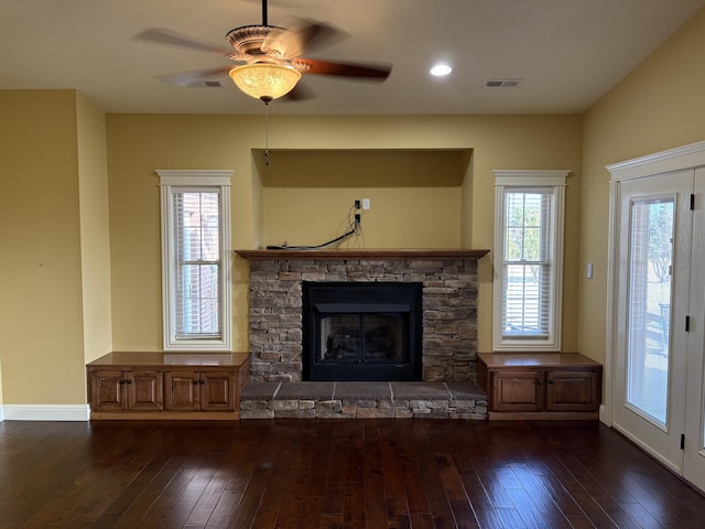 unfurnished living room with a stone fireplace, dark wood-type flooring, and ceiling fan