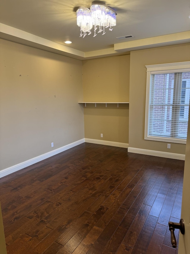 spare room with dark wood-type flooring and a chandelier