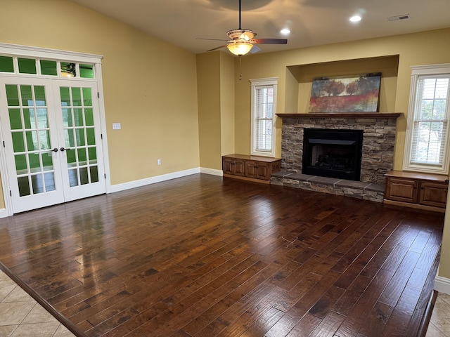 unfurnished living room featuring french doors, ceiling fan, wood-type flooring, and a stone fireplace