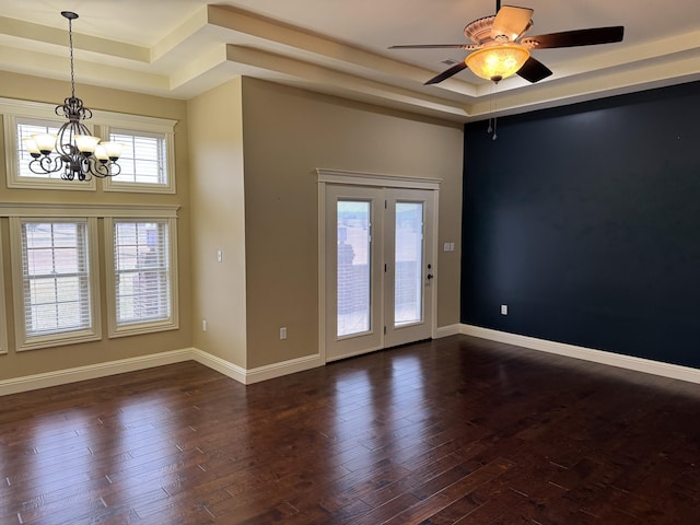 empty room featuring a tray ceiling, ceiling fan with notable chandelier, and dark hardwood / wood-style floors