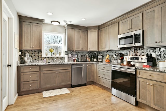 kitchen featuring appliances with stainless steel finishes, sink, decorative backsplash, light hardwood / wood-style floors, and light stone countertops