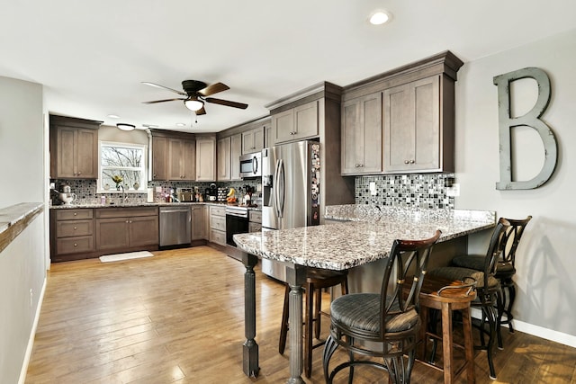 kitchen with sink, light stone counters, appliances with stainless steel finishes, kitchen peninsula, and light hardwood / wood-style floors