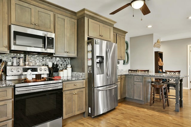 kitchen with appliances with stainless steel finishes, a kitchen breakfast bar, decorative backsplash, and dark stone countertops