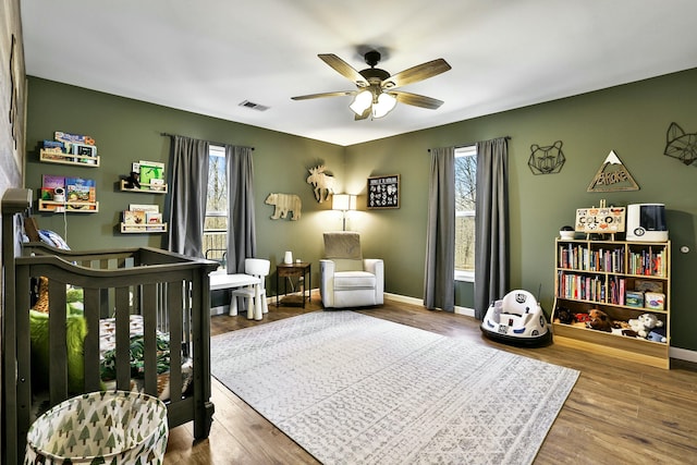 bedroom with multiple windows, hardwood / wood-style floors, a crib, and ceiling fan